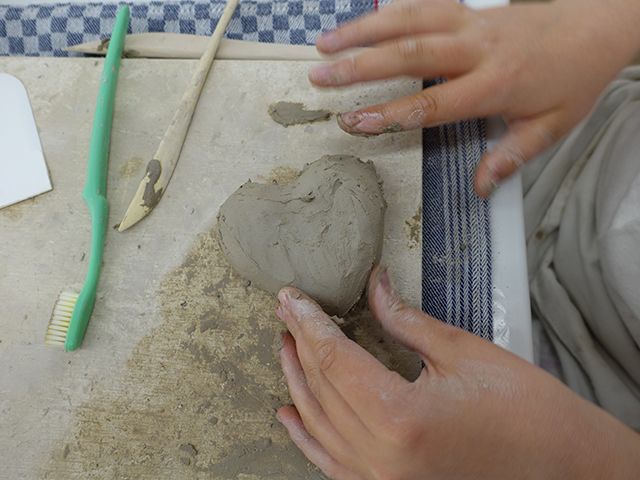 Kind modelliert ein Herz mit Ton.